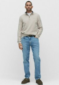 Ljust grå zip-up tröja, blå jeans och bruna skor. Tröjan har en krage och en liten logo. Jeans är raka med en urtvättad look.