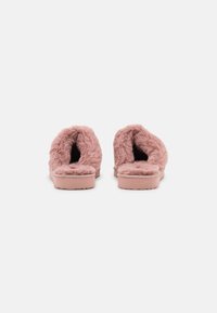 Mjuk rosa tofflor med en plyschig, fluffig textur, öppen baksidesdesign och platta sulor för komfort. Anmärkningsvärd tjock inre foder och kuddad fotbädd.