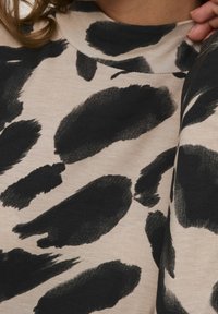 Sweatshirt beige avec un motif de coups de pinceau noir, col rond et texture de tissu douce. La vue en gros plan met en évidence les détails du design.