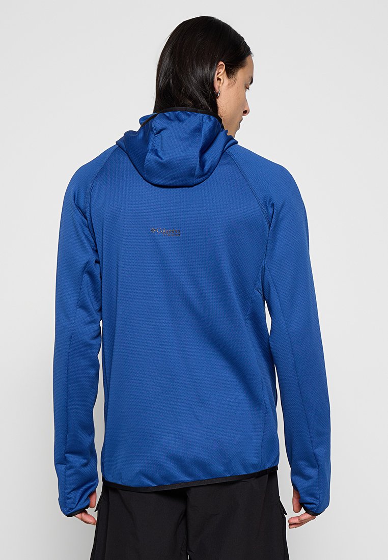 Veste à capuche bleue en tissu texturé, avec une coupe ajustée et un accent logo au dos. Convient pour les activités de plein air.