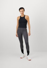 Crni sportski crop top s prednim patentnim zatvaračem, uparen s uskim sivim tajicama s naglašenim šavovima i crnim gležnjačama. Bijeli tenisice.