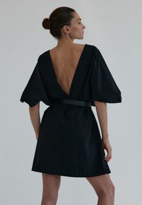 Czarna sukienka z głębokim dekoltem na plecach, krótkimi falbanowymi rękawami i dopasowaną talią. Wykonana z lekkiego materiału o gładkiej fakturze.