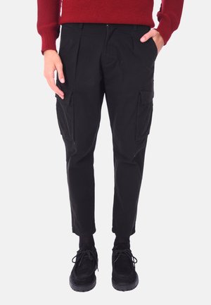 Pantaloni cargo neri con vestibilità affusolata, dotati di tasche laterali e un tessuto liscio e resistente. Indossati con scarpe in camoscio nere.