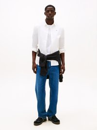 Hvit skjorte med knapp, grå genser knyttet rundt livet, blå rette jeans, svarte joggesko med tekstur.