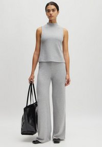 Grijze geribbelde gebreide twee-delige outfit bestaande uit een mouwloze top met hoge hals en wijde broek, aangevuld met een zwarte tote bag.