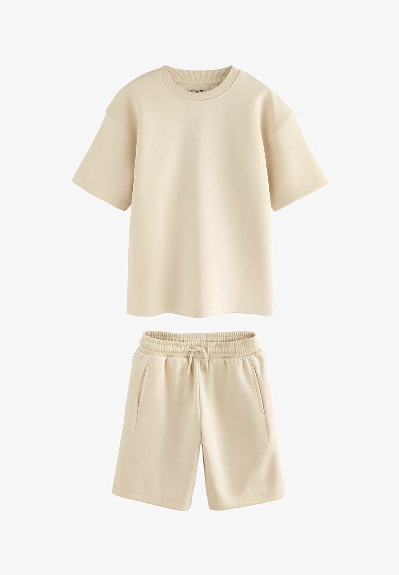 T-shirt beige à manches courtes et col rond, associé à un short taille élastique avec cordon de serrage et poches latérales.