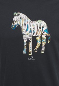 Mustassa t-paidassa on värikäs, kuvioitu seeprahahmo, jossa on yksityiskohtaisia tekstuureja ja sävyjä, ja joka on varustettu "PS" ja "Paul Smith" -tekstillä.