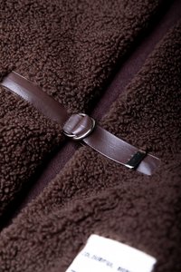 Brun fleece tyg med en mjuk, texturerad yta, med ett brunt läderrem och detaljer i silver för fastsättning.
