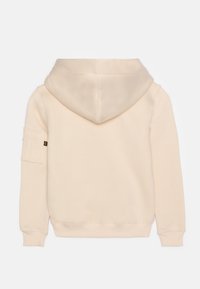 Felpa beige con una consistenza morbida, caratterizzata da un grande cappuccio e una tasca a toppa sul braccio sinistro. Design semplice, senza grafiche visibili.