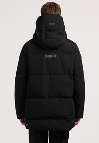 Pūkinė striukė vientisos juodos spalvos, su dideliu gobtuvu, siūtu raštu ir atspindinčia detalė nugarėlėje. Ilgos apimties ir ilgi rankogaliai.