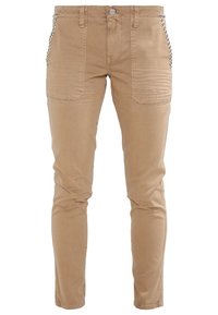 Pantalons en denim ajustés couleur tan, dotés de poches latérales, de coutures décoratives et de clous décoratifs le long des bords des poches.