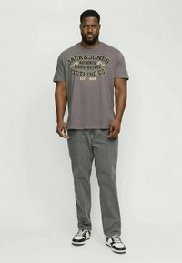 Grå t-shirt med svart och gul text, kombinerad med gråjeans och svart-vita sneakers. Enkelt mönster, kort ärm, avslappnad passform.