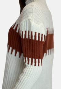 Bomullströja med ribbat mönster, vita och rostfärgad färgblock, samt ett distinkt zigzag-mönster längs axelsömmarna.