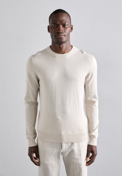 Krèmefarvet strikket sweater med rund halsudskæring og ribbede manchetter, der har en blød tekstur og tætsiddende design.