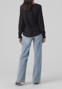 Maglietta nera con texture a maniche lunghe abbinata a jeans blu chiaro a vita alta e gamba dritta. La maglia presenta polsini arricciati e orlo arrotondato.