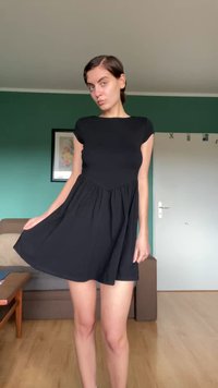 Čierne šaty s krátkym rukávom, s priliehavým telom a rozšírenou sukňou, vyrobené z hladkého materiálu. Sukňa má zberanú dekoráciu v páse.