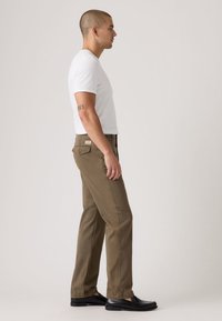 Χακί παντελόνι με ίσια γραμμή, κατασκευασμένο από βαμβάκι, με πλαϊνές τσέπες και μια πίσω τσέπη με ετικέτα. Φορεμένο με απλό λευκό μπλουζάκι.