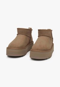 Bruine suède enkellaarsjes met een ronde neus, platte plateauzool en stikdetails. Voorzien van een lusje om ze gemakkelijk aan te trekken.