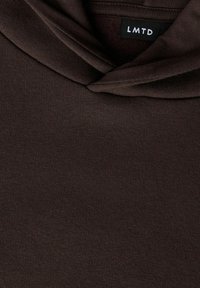 Smeđi pulover od mekog, teksturiranog tkanja. Ima ovratnik u obliku okruglog vratnog dijela i oznaku s natpisom "LMTD" blizu ovratnika.