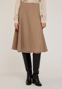 Una gonna a trapezio di lunghezza al ginocchio in tessuto marrone chiaro con una trama liscia, abbinata a stivali neri alti, lucidi, in pelle stampata coccodrillo.