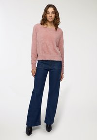 Maglione lavorato a maglia di un rosa chiaro e soffice, con scollatura rotonda e maniche lunghe, abbinato a jeans in denim scuro a gamba larga; stivali neri alla caviglia.