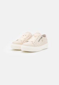 Beige lavtop sneakers med quiltet sideskpanel, snørebånd fortil, en udvendig lynlåsdetaile og hvide platformssåler på en hvid baggrund.