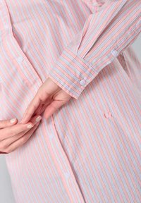 Lightweight, striped shirt featuring alternating pink and light blue vertical lines, with button closure and cuff detailing.