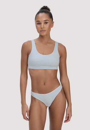 Woman with tied-up hair wearing a light blue and white striped bikini, standing against a plain light background.