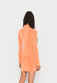 Vestido justo de mangas longas em tecido laranja texturizado, com colarinho e punhos com fenda. Corte até a metade da coxa, superfície lisa com um brilho sutil.