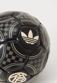 Mustan värviga jalgpall, mis on valmistatud sünteetilisest materjalist ja millel on tekstureeritud pind, kullatooniliste aksessorite, ruuduliste mustrite ja Adidas logo kujutisega.
