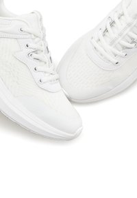 White athletic shoes featuring a textured mesh upper, round laces, padded collar, and a cushioned white rubber sole.