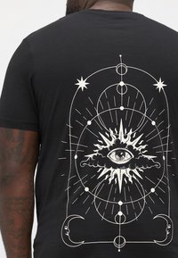 Black t-shirt featuring a large white graphic on the back, depicting an eye within a sunburst design, surrounded by celestial elements.