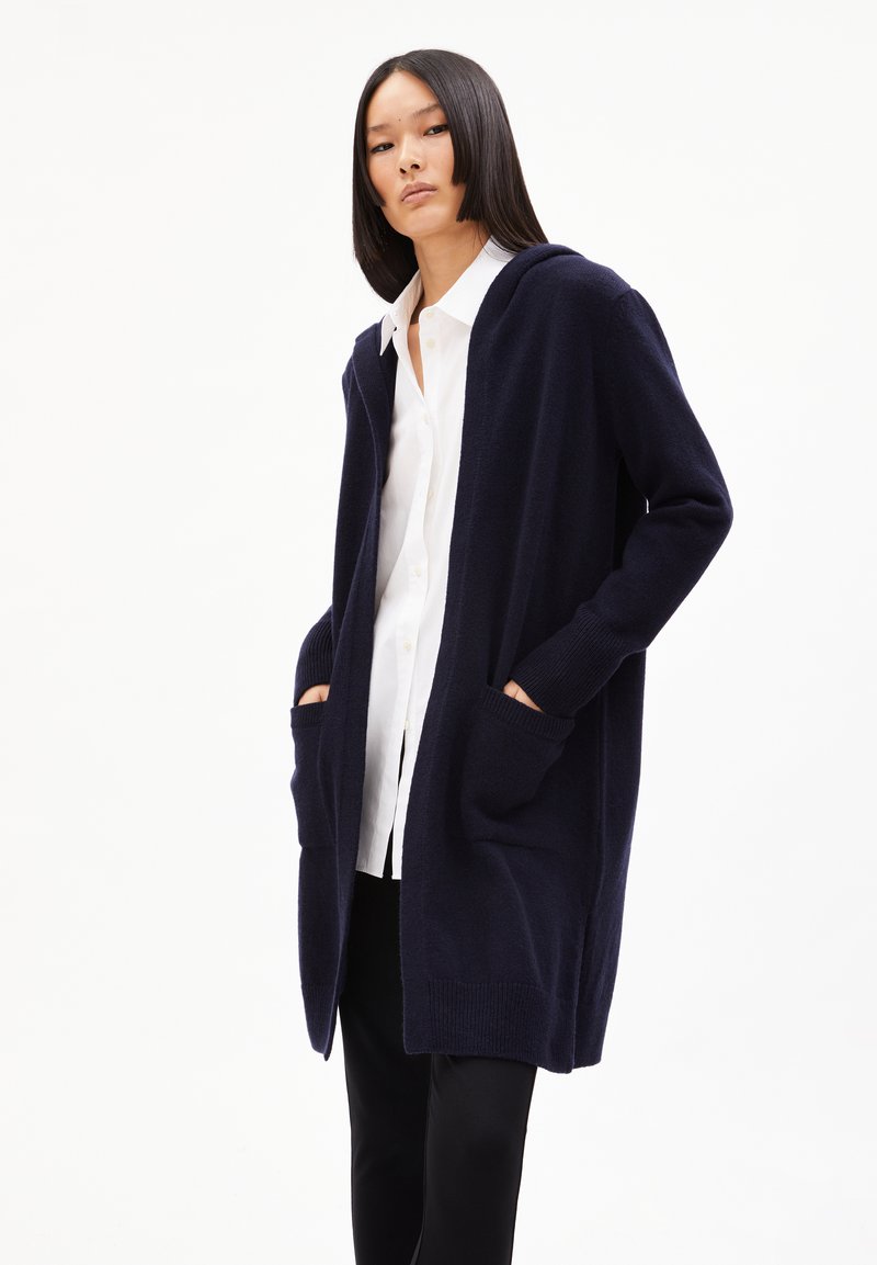 Cardigan bleu marine en tissu tricot doux, doté d'une capuche, de manches longues, de poches avant et d'un design ouvert.