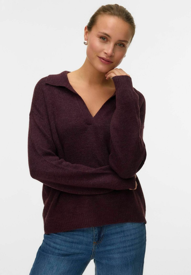 Maglione bordeaux a maglia con scollo a V e colletto ampio, caratterizzato da polsini a coste. Abbinato a jeans di denim, che mostrano una vestibilità comoda.