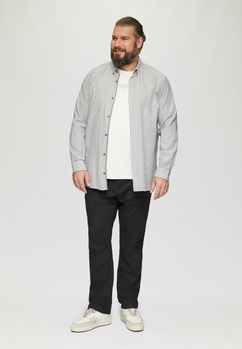 Chemise à boutons avec des rayures bleu et blanc, superposée à un t-shirt blanc ; associée à un pantalon noir et des baskets blanches.