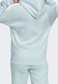 Sweat à capuche bleu clair en tissu doux, avec une poche kangourou, des poignets côtelés et une capuche à cordon. Le dos présente une texture lisse.