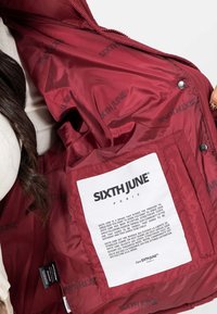 Burgundy jacka med glänsande finish, med en inre etikett. Mönstrad med "SIXTH JUNE"-logotyper på foderet. Strukturerat tyg.