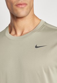 Helle olivgrüne Nike T-Shirt mit Rundhalsausschnitt, weichem Stoff und schwarzem Nike-Swoosh-Logo auf der linken Brust.
