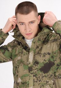 Jachetă de camuflaj în tonuri de verde și maron, cu guler înalt, glugă cu șnur și închidere cu fermoar. Material texturat cu un design pattern.