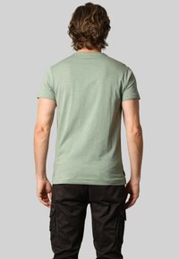 T-shirt vert à manches courtes avec une texture douce. Design simple, coupe ajustée et encolure plate. Porté avec un pantalon cargo sombre.