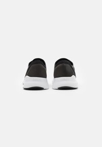 Une paire de baskets Lacoste noires et blanches vue de l'arrière, avec des semelles intermédiaires blanches texturées et des semelles extérieures noires.