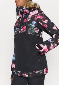 Giacca con motivo floreale caratterizzata da tessuto nero con dettagli di fiori rosa e verdi, cappuccio foderato in pelliccia e polsini delle maniche regolabili.