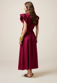 Marlowe jurk in donker bordeaux, met een ontwerp van ruches aan de mouwen, een cinched taille en een vloeiende rok. Soepele textuur en enkel-lang.