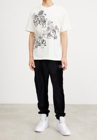 Camiseta blanca de manga corta con un estampado gráfico negro. Combinada con pantalones de pana negros y zapatillas blancas. Ajuste simple y relajado.
