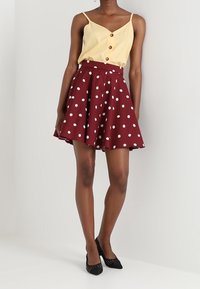 Burgundy prickigt kjol med en utsvängd design, kombinerad med en gul knappad linne. Kjolen har en mjuk textur och är medellång.