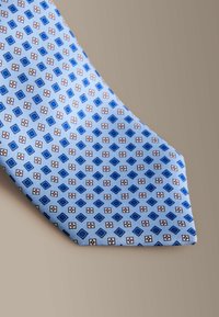 Blåt mønstret slips med et design af blå firkanter og røde kanter på en lyseblå baggrund. Glat tekstur med klassisk form.