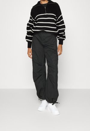 Svart och vit randig stickad tröja med halvmångzipped krage, i kombination med lösa svarta cargobyxor och vita sneakers.