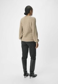 Be�żowy sweter dzianinowy o prążkowanej teksturze, z długimi, bufiastymi rękawami i ukośnym detalem szwu, w połączeniu z czarnymi dopasowanymi dżinsami i bootsami do kolan.