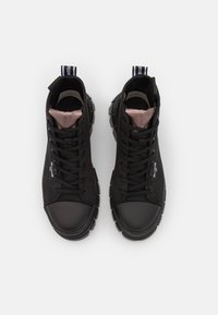 Baskets noires montantes avec un dessus texturé, embout rond en caoutchouc et semelle épaisse. Elles présentent des lacets noirs et une doublure rose contrastante.
