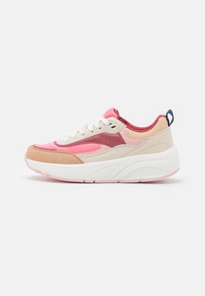 Zapatilla deportiva rosa y beige con paneles de ante y malla, cordones blancos y una suela blanca gruesa. Presenta una pequeña etiqueta azul en el talón.